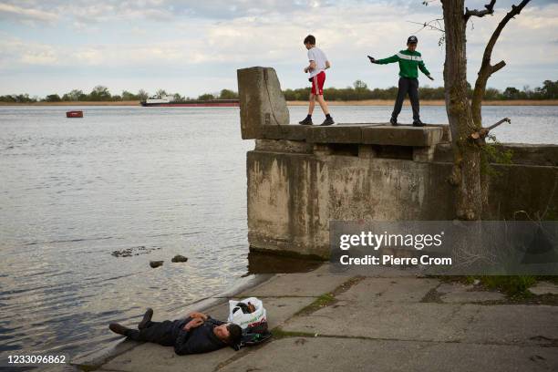 Children play on a wall as a man sleeps on the bank of the Dnieper River on May 3, 2021 in Kherson, Ukraine.