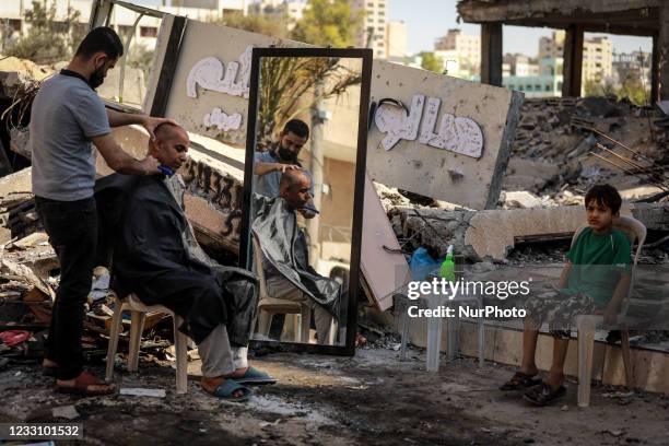 Palestinian barber works next to the ruins of buildings and shops destroyed by Israeli strikes, in Gaza City, on May 25, 2021. - A ceasefire was...