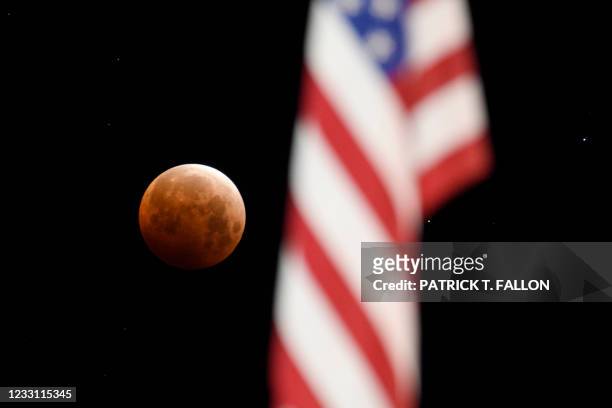 Full moon is seen framed with a US flag during totality of a total lunar eclipse as the moon enters Earth's shadow for a "Super Blood Moon" on May...