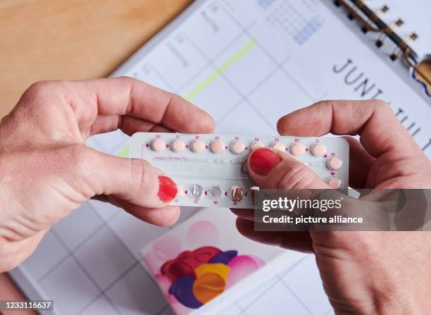 May 2021, Berlin: Above a calendar, a woman takes the next pill from the monthly pack of the contraceptive pill. The birth control pill went on sale...