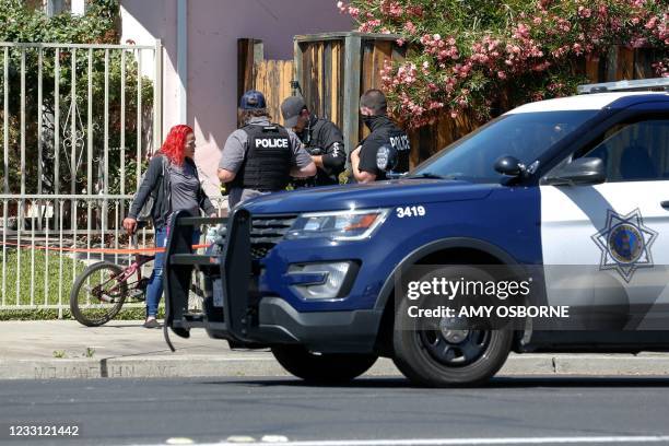 Police officers speak with a local resident as emergency responders respond to a fire at the house of the suspect of a shooting, after nine people...