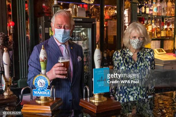Prince Charles, Prince of Wales pulls a pint of beer in a pub alongside Camilla, Duchess of Cornwall during a visit to Clapham Old Town on May 27,...
