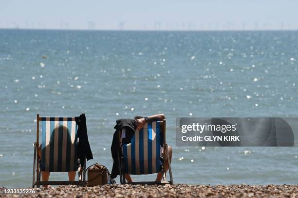 People sit in deckchairs looking out onto the channel on Brighton beach in Brighton, southern England as temperatures rise across the country on May...