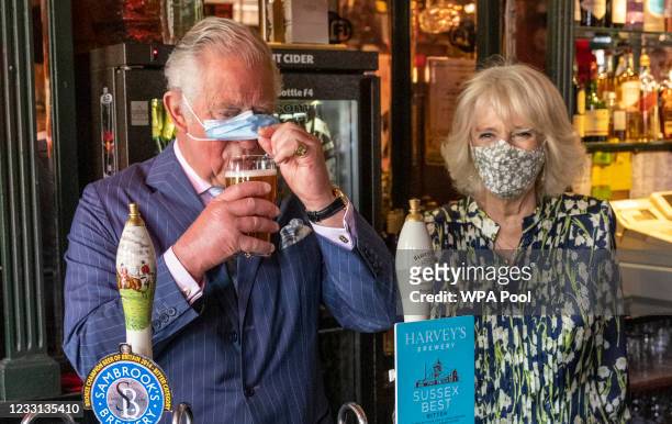 Prince Charles, Prince of Wales adjusts his face mask to enable him to sip a pint that he pulled in a pub alongside Camilla, Duchess of Cornwall...