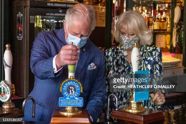 Britain's Prince Charles, Prince of Wales pulls a pint of Sambrook's Brewery 'Wandle' beer as Britain's Camilla, Duchess of Cornwall looks on during...
