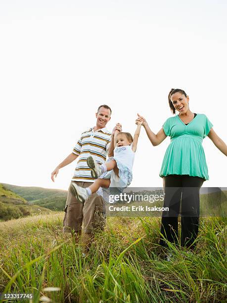 happy parents swinging daughter in field - mom flirting stock pictures, royalty-free photos & images