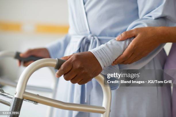 nurse helping woman use walker in hospital hallway - looprek stockfoto's en -beelden