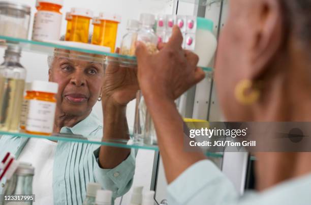 black woman taking medication from cabinet - badezimmerschrank stock-fotos und bilder