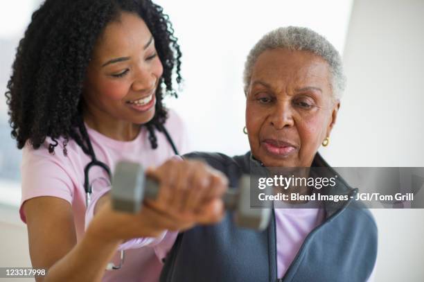 nurse helping woman exercise with dumbbell - senior physiotherapy stock pictures, royalty-free photos & images