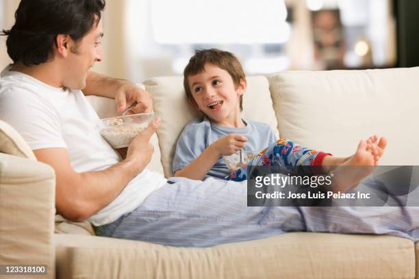 caucasian father and son eating cereal together on sofa - boy eating cereal stock pictures, royalty-free photos & images