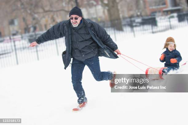 grandfather pulling grandson on sled in snow - grandfather child snow winter stock pictures, royalty-free photos & images