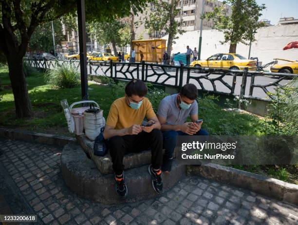 Two Iranian men wearing protective face masks use their smartphones while sitting on a street-side in downtown Tehran on May 30, 2021. Iranians will...