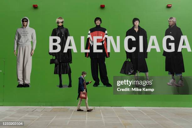 People interact with large scale action figures wearing fashionable clothing against a huge green hoarding which covers the Balenciaga store during a...