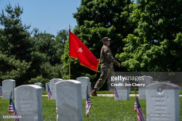 Soldier in uniform walks past headstones and American flags in the Fort Knox Main Post Cemetery on May 31, 2021 in Fort Knox, Kentucky. The cemetery...