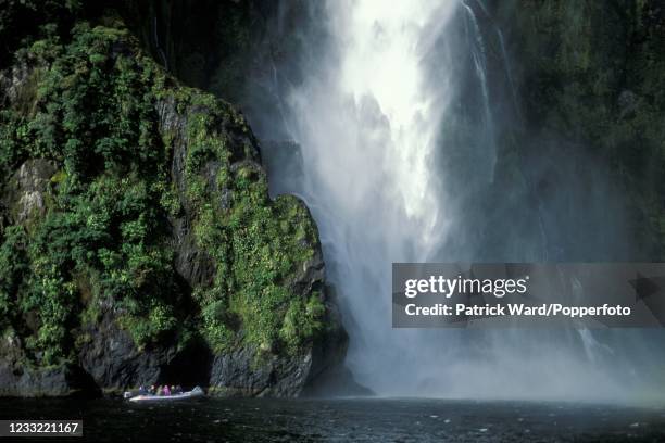 Tourists from the overnight "Wanderer" boat trip on Milford Sound approaching a waterfall in the ship's tender on the South Island of New Zealand,...