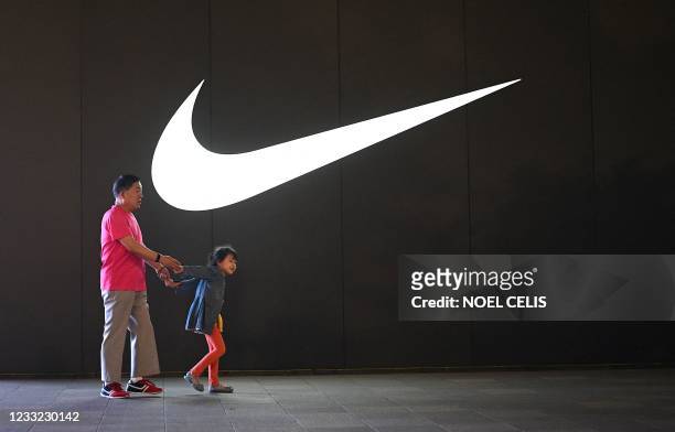 An elderly man and a child walk past a Nike logo in Wangfujing shopping district in Beijing on June 2, 2021.
