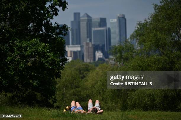 People enjoy the sunshine with the view of the City of London skyline in the background, in Greenwich Park, south east London on June 3, 2021. - Much...