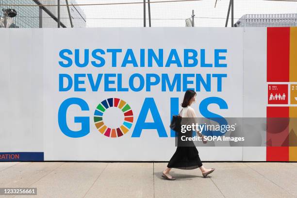 Woman wearing a mask as a preventive measure against the spread of covid-19 walks past a sign advertising UN's 'Sustainable development goals' in...