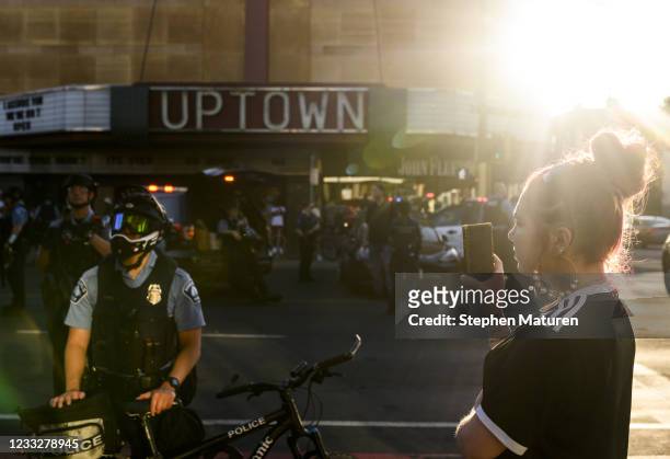 Woman holds up her phone as Minneapolis Police hold a line while they clear an intersection where people were demonstrating for Winston Boogie Smith...