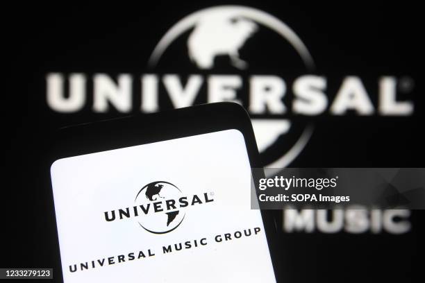 In this photo illustration, Universal Music Group logo is seen on a smartphone and pc screen.