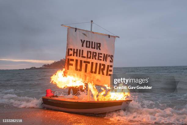 Ocean Rebellion staged a theatrical action with a Boris Johnson head and an Oilhead sitting in deckchairs on Marazion beach while a boat burns in the...