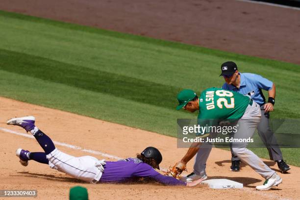 Brendan Rodgers of the Colorado Rockies dives safely back into first base ahead of the throw to Matt Olson of the Oakland Athletics as first base...