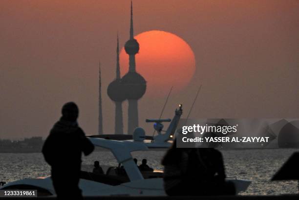 People watch the sunset behind the Kuwait Towers in Kuwait City on June 7, 2021.