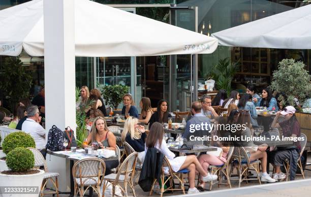 People eat and drink at outside tables as they enjoy the warm weather on the South Bank in central London, following the further easing of lockdown...