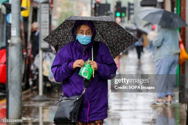 Woman wearing a face mask shelters from the rain beneath an umbrella during a rainfall in London.