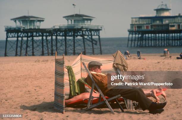 Relaxing on the beach at Skegness in Lincolnshire, with the derelict Pier behind, circa July 1990.