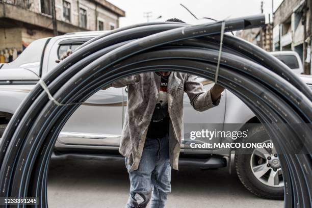 Man rolls a bundle of pipes as he crosses a street in the historical Merkato area of Addis Ababa on June 11, 2021. - Most of Ethiopia is heading to...