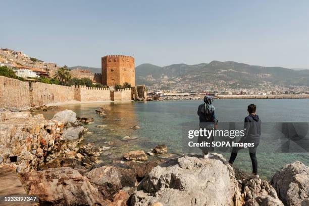 Turkish tourists enjoy the view of the ancient walls of Alanya castle and the Red Tower on the Mediterranean coast. The Turkish seaside resort of...