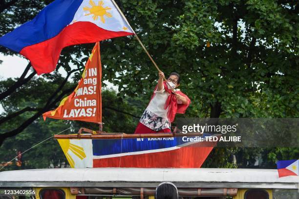 Protester waves a Philippine national flag on a makeshift wooden fishing boat atop a passenger jeepney prior to their motorcade protest at the...