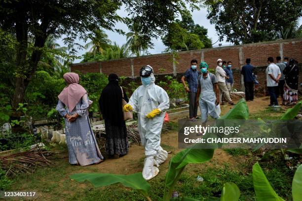 Gravedigger wearing protective gear walks past family members after burying a victim of the COVID-19 coronavirus at the municipal cemetery in Banda...