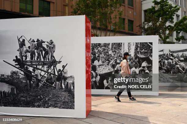 Woman walk past an exhibit of cultural revolution pictures along Wangfujing shopping district in Beijing on June 12 ahead of the 100th anniversary of...