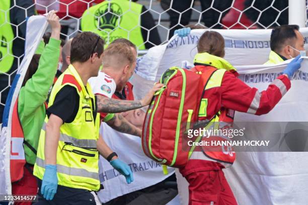 Denmark's defender Simon Kjaer checks on Denmark's midfielder Christian Eriksen as paramedics carry him on a stretcher after collapsing during the...