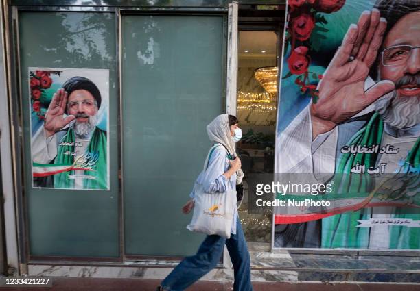 An Iranian woman wearing a protective face mask walks past presidential elections candidate Ebrahim Raisis electoral banners that are hanged out of a...