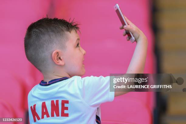 Boy wearing a jersey of England's forward Harry Kane uses a smartphone before the start of the UEFA EURO 2020 Group D football match between England...