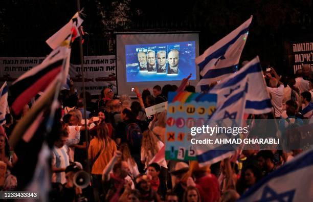 Israeli demonstrators gather near a screen showing a projection of the faces of the heads of a new coalition government, Naftali Bennett of Yamina,...