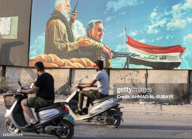 Men ride scooters past a billboard depicting the late commander of the Iranian-backed Hashed al-Shaabi paramilitary forces Abu Mahdi al-Muhandis and...