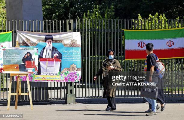 Iranians walk past banners encouraging people to vote hung on a fence at Tehran university in the eponymous capital, on June 14 ahead of the June 18...
