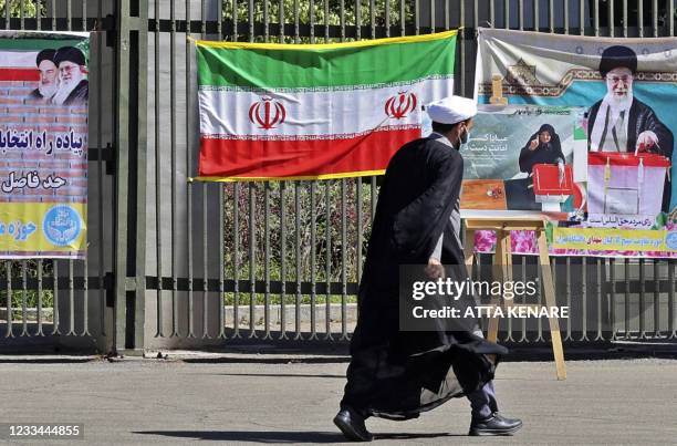 An Iranian man walks past national flags and banners encouraging people to vote hung on a fence at Tehran university in the eponymous capital, on...