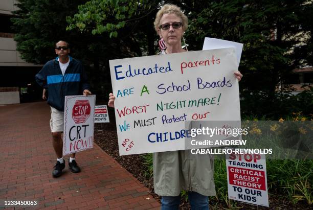 People hold up signs during a rally against "critical race theory" being taught in schools at the Loudoun County Government center in Leesburg,...