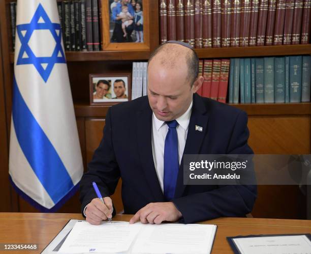 Israel's new Prime Minister Naftali Bennett signs a letter as he began his term as the new prime minister at the Prime Minister's Office in West...