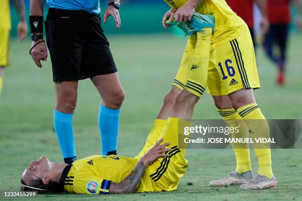 Sweden's midfielder Kristoffer Olsson is helped by a teammate as he has muscle pains during the UEFA EURO 2020 Group E football match between Spain...