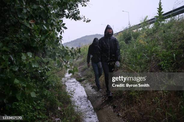 An Algerian and a Palestinian asylum seeker walk through the woods in a downpour near the side of a highway as they crossed into Greece from from...