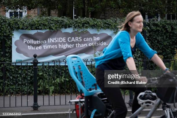 Woman cyclist passes a pollution awareness banner that is attached to the railings of Dulwich Hamlet School, where restrictions also prevent traffic...