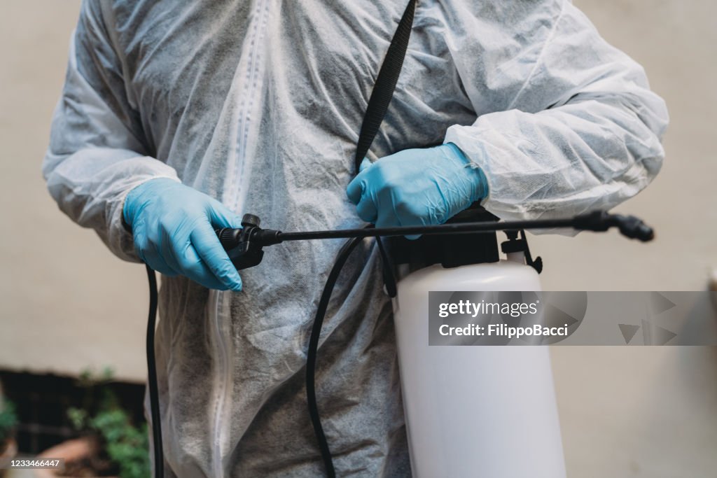 Detail of a sanitation worker in protective suit holding a sprayer