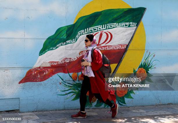 An Iranian woman walks past a mural displaying Iran's national flag in Tehran, on June 17 on the eve of the Islamic republic's presidential election.