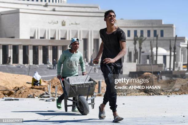 Workmen transport a wheelbarrow while behind is seen ongoing construction work at Egypt's new parliament headquarters being built at the "New...